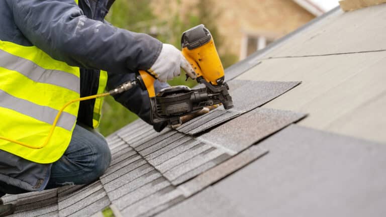 Workman using pneumatic nail gun install tile on roof of new hou